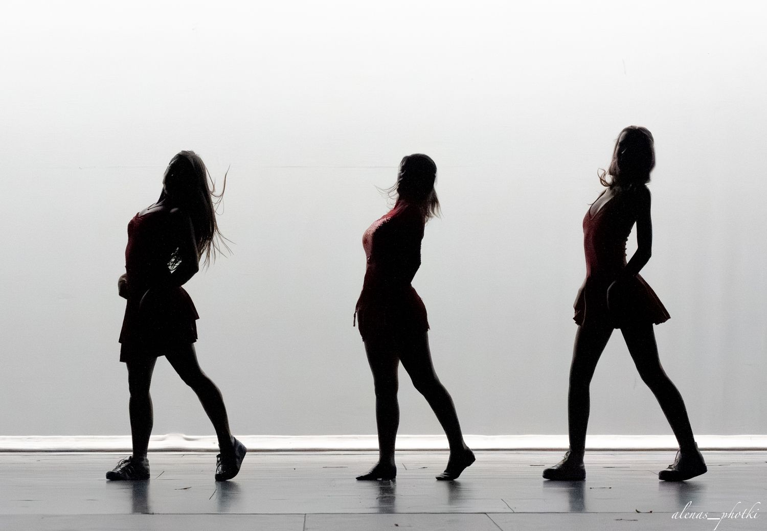 Three women in black outfits strike dynamic poses in silhouette against a white background.