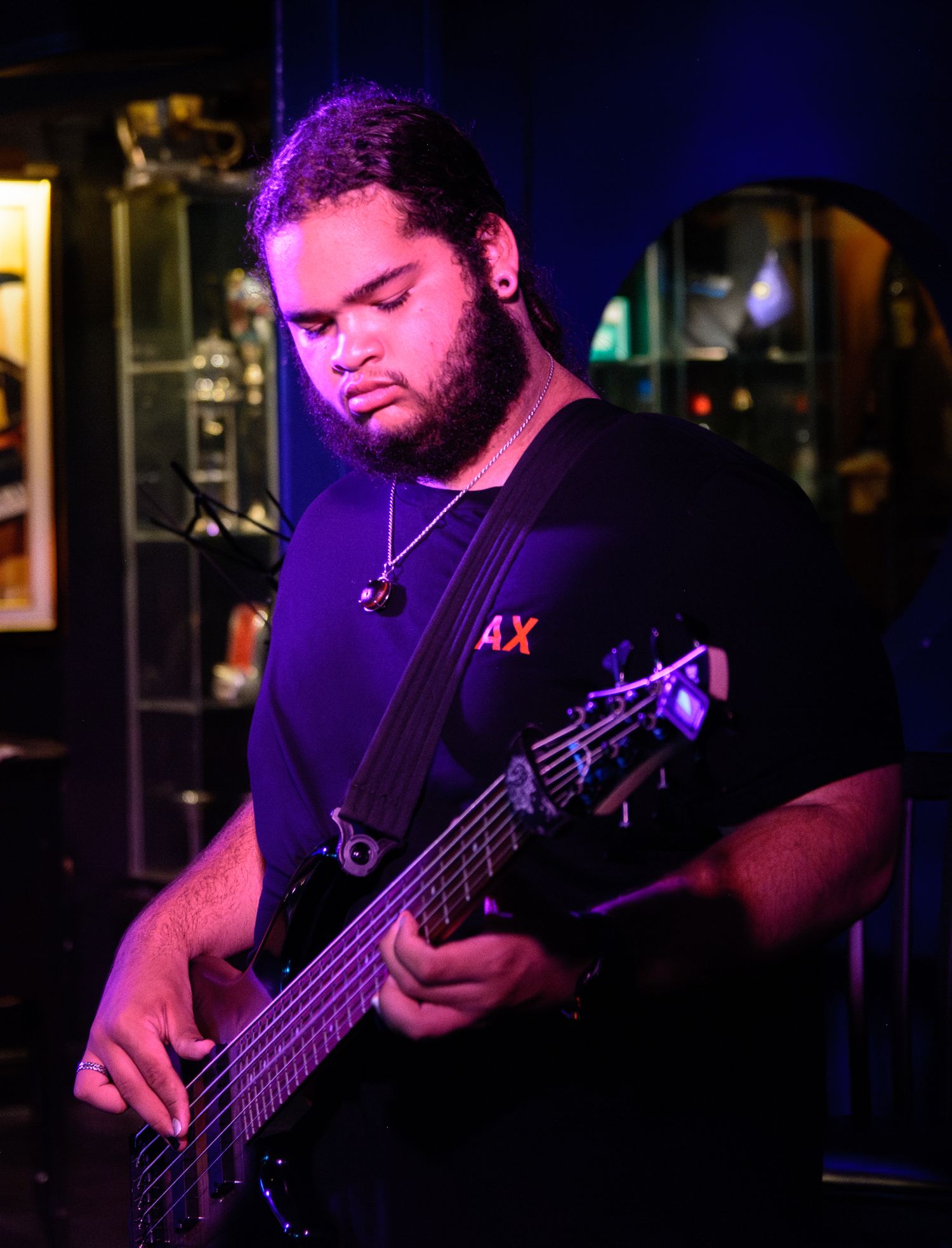 Bass guitarist performing on stage with purple lighting in a dark bar setting.