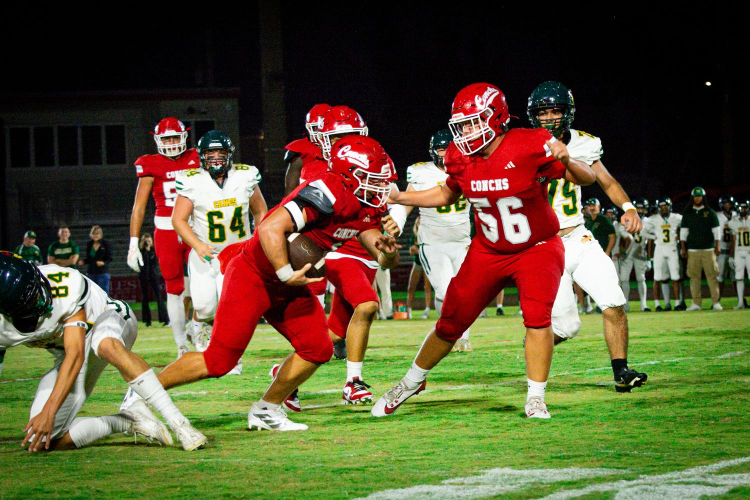 Football players in red uniforms engage in a ground play during a night game.