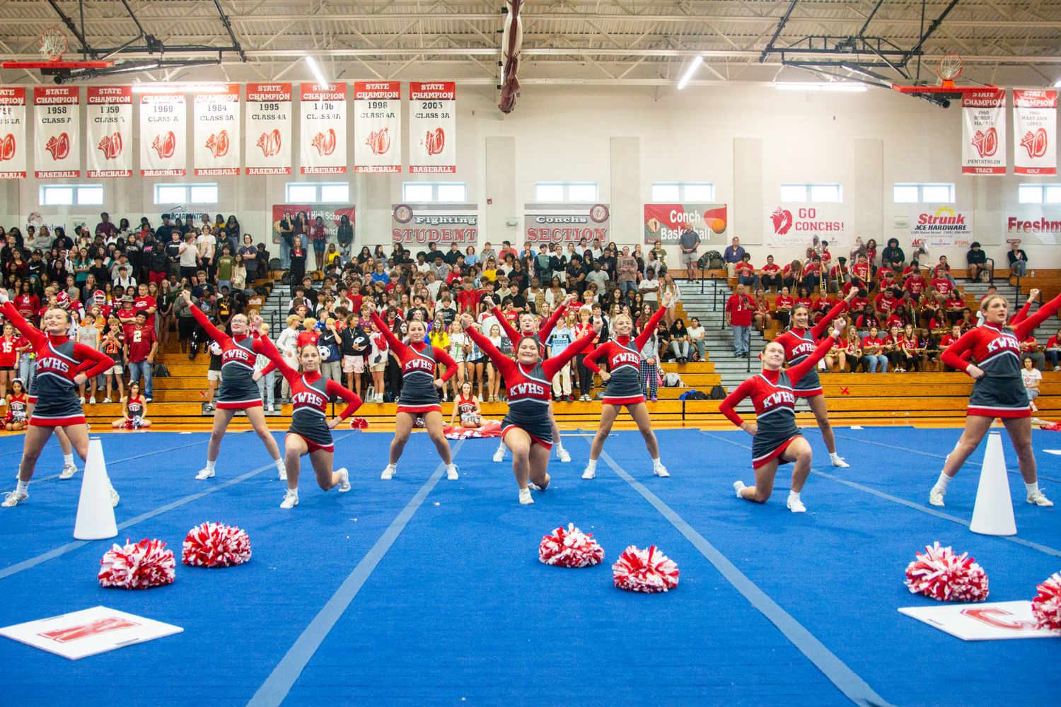 Cheerleaders perform synchronized routine on blue mats at an indoor competition.