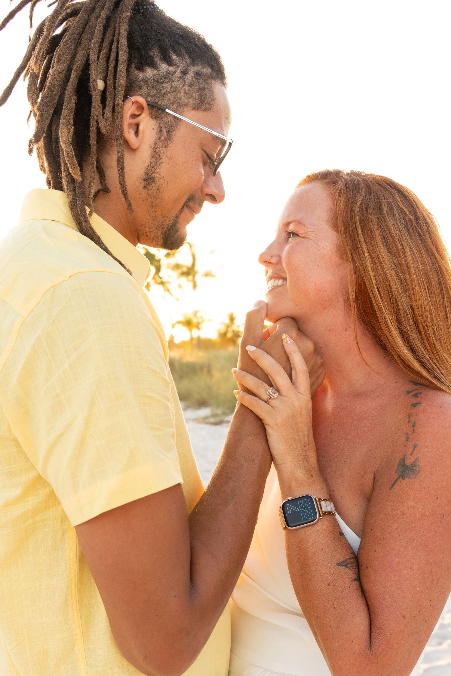 Happy interracial couple holding hands and smiling at each other during a golden hour beach session.