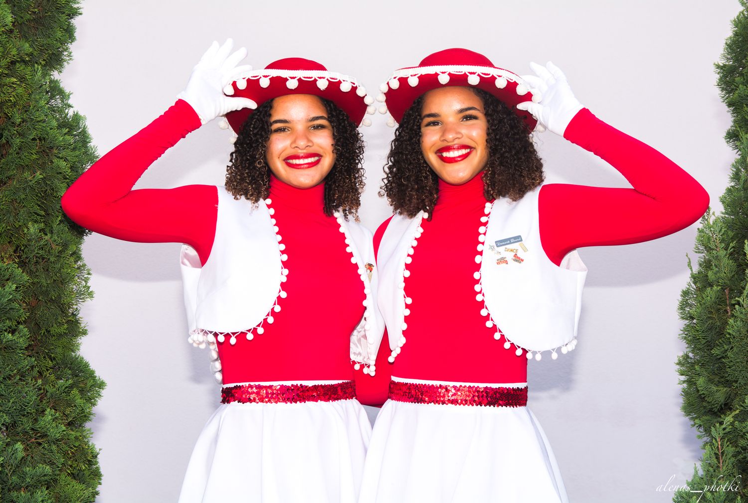 Two matching cheerleaders in red and white uniforms with decorative red hats pose together against a white backdrop.