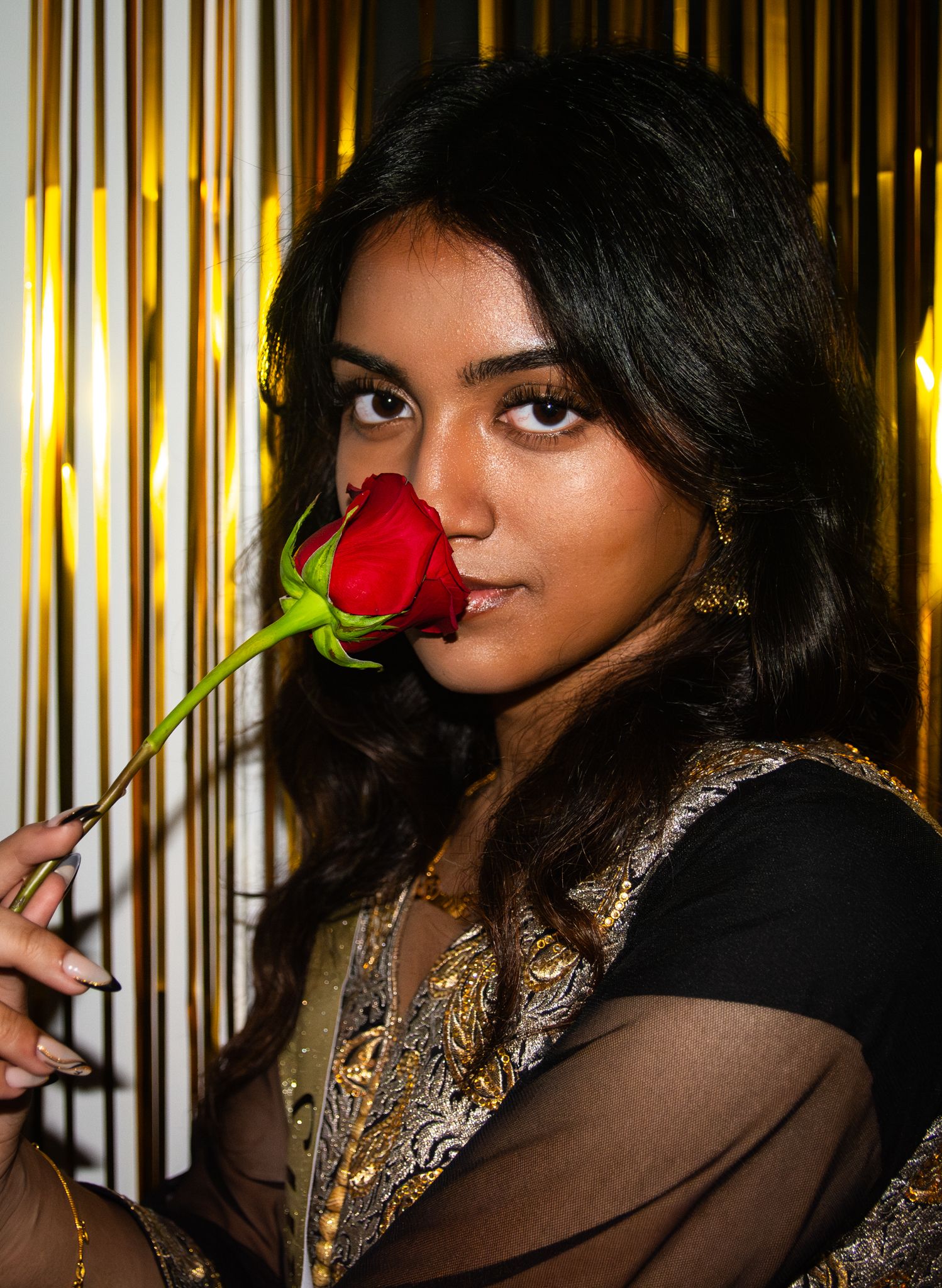 A figure holds a red rose against a gold striped background.