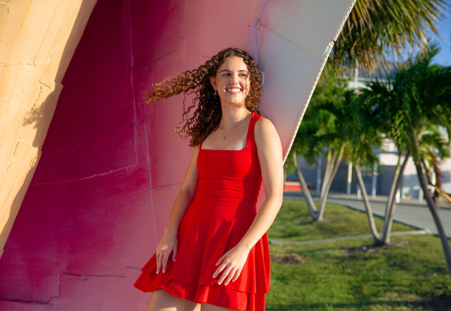 Vibrant red dress contrasts against colorful architectural backdrop with palm trees.