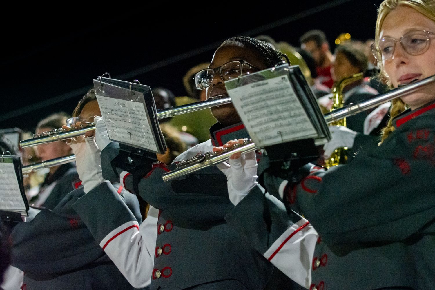 Flute players in black uniforms perform during a nighttime marching band show.