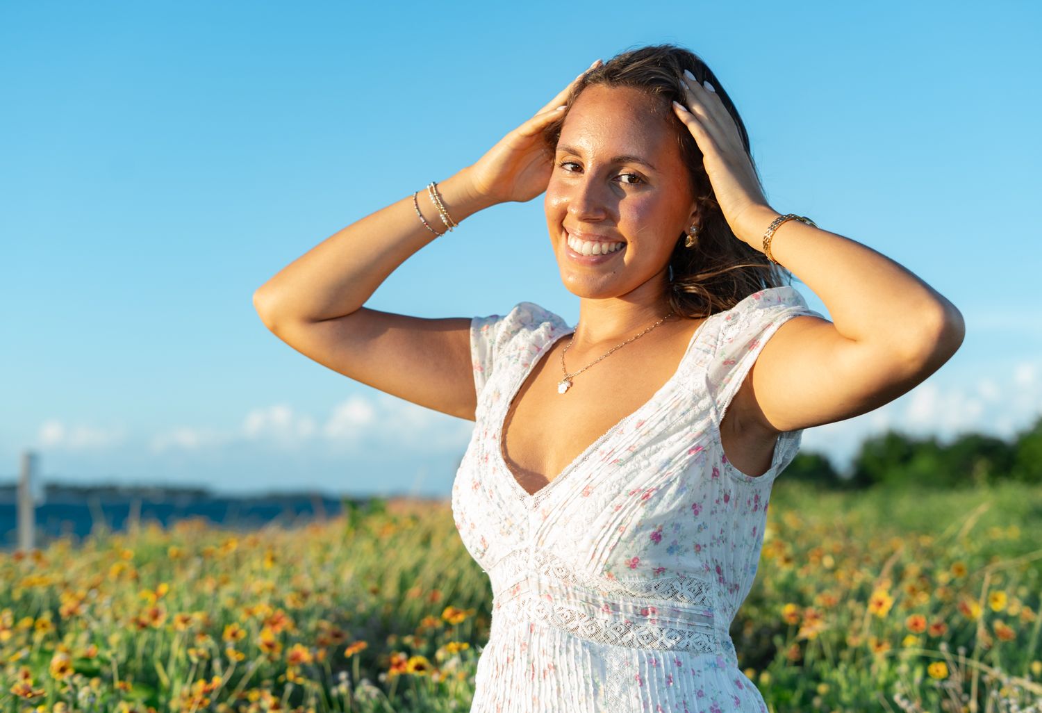 A woman in a white sundress poses joyfully in a vibrant field of yellow wildflowers under bright blue summer skies.
