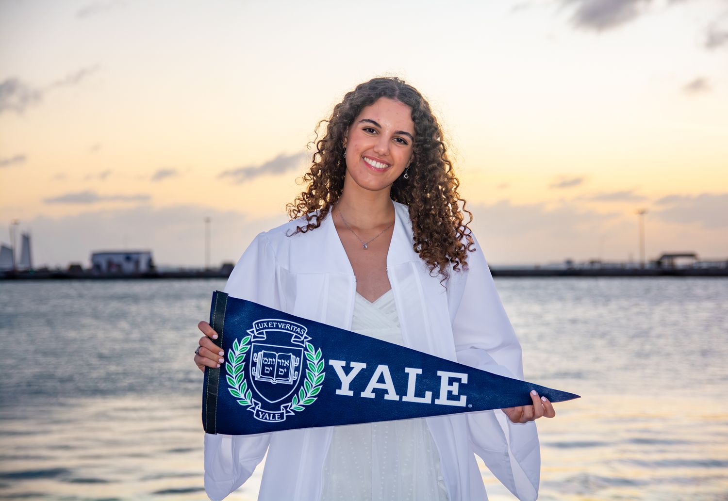 Graduate displays Yale University pennant at sunset by waterfront.
