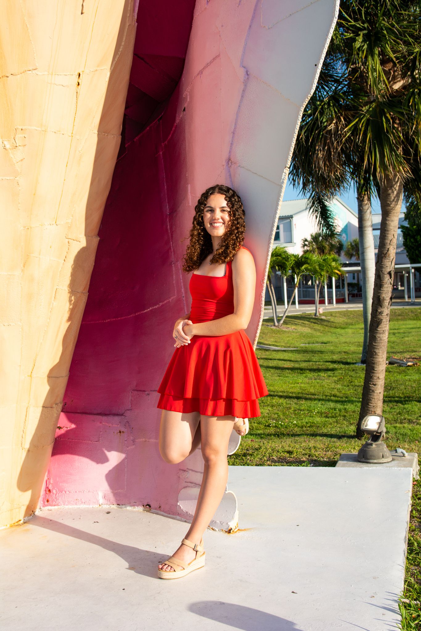 Red ruffled skirt twirls against pink wall and palm trees in tropical setting.