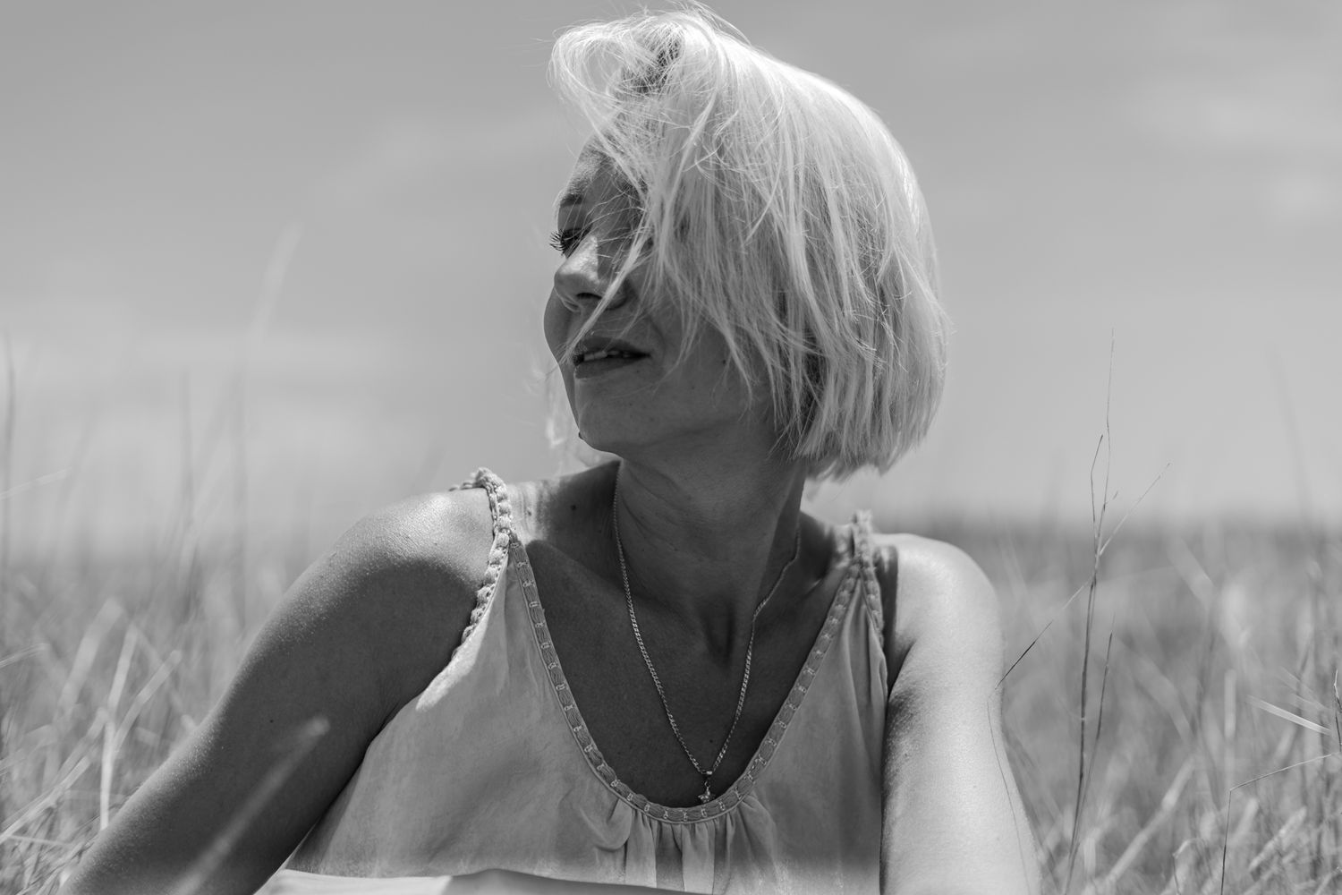 A candid black and white portrait of someone enjoying a sunny day in tall grass.
