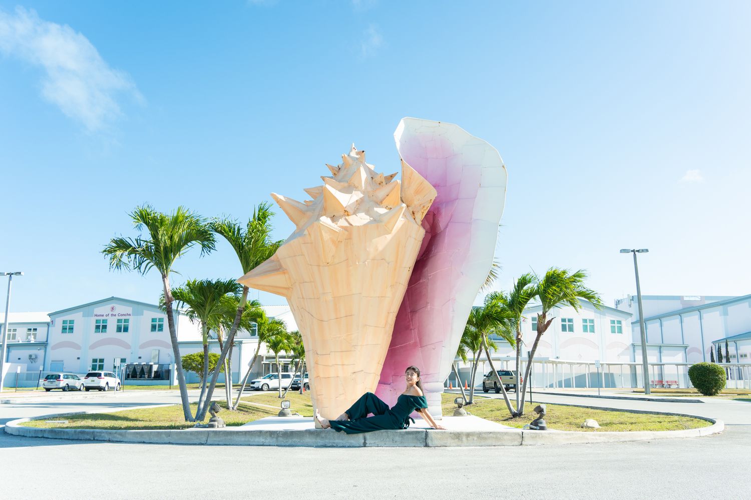 Giant conch shell sculpture landmark in a sunny tropical setting with palm trees and blue sky.