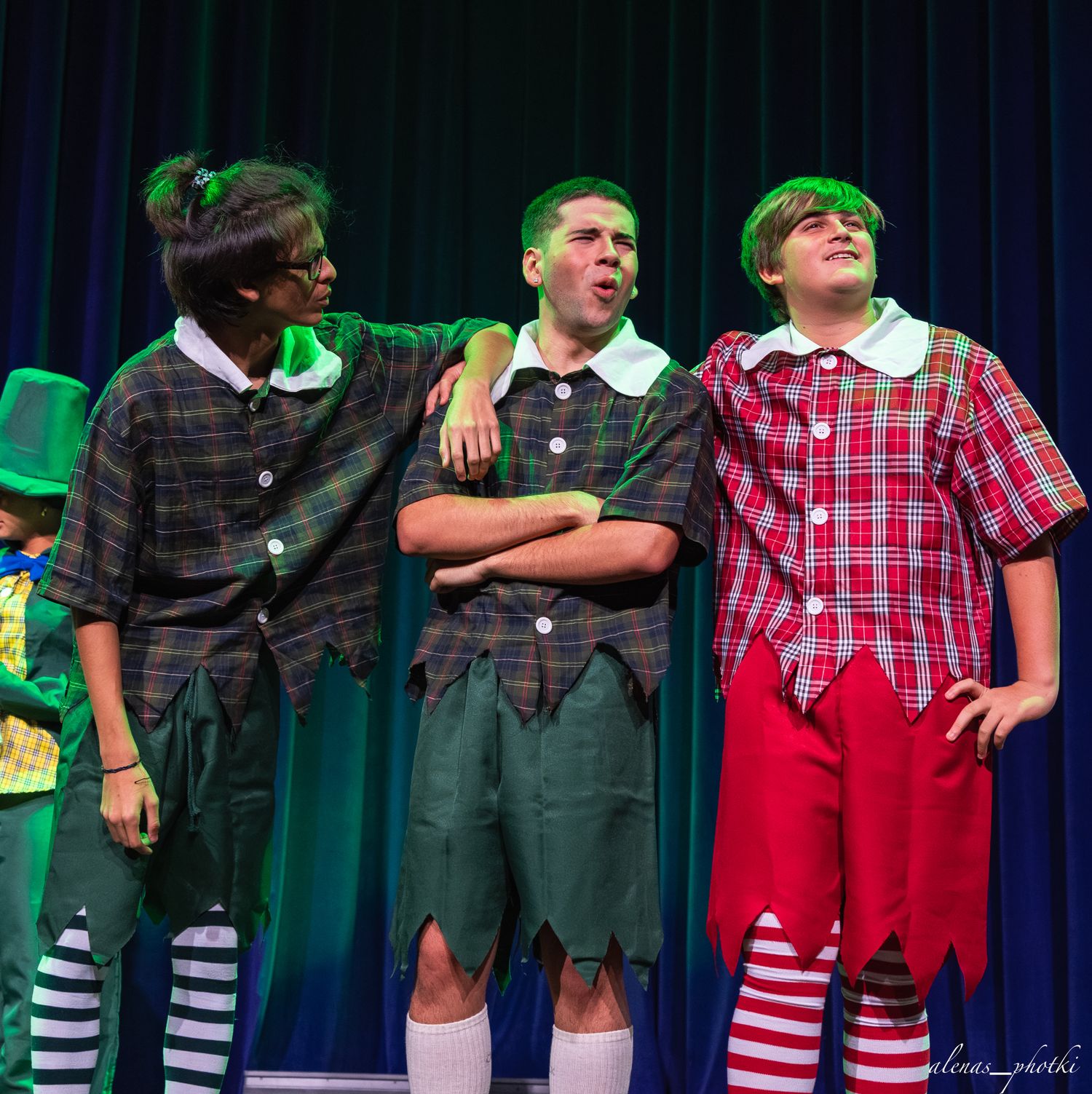 Students in colorful costumes and striped socks perform in a theatrical production on stage.