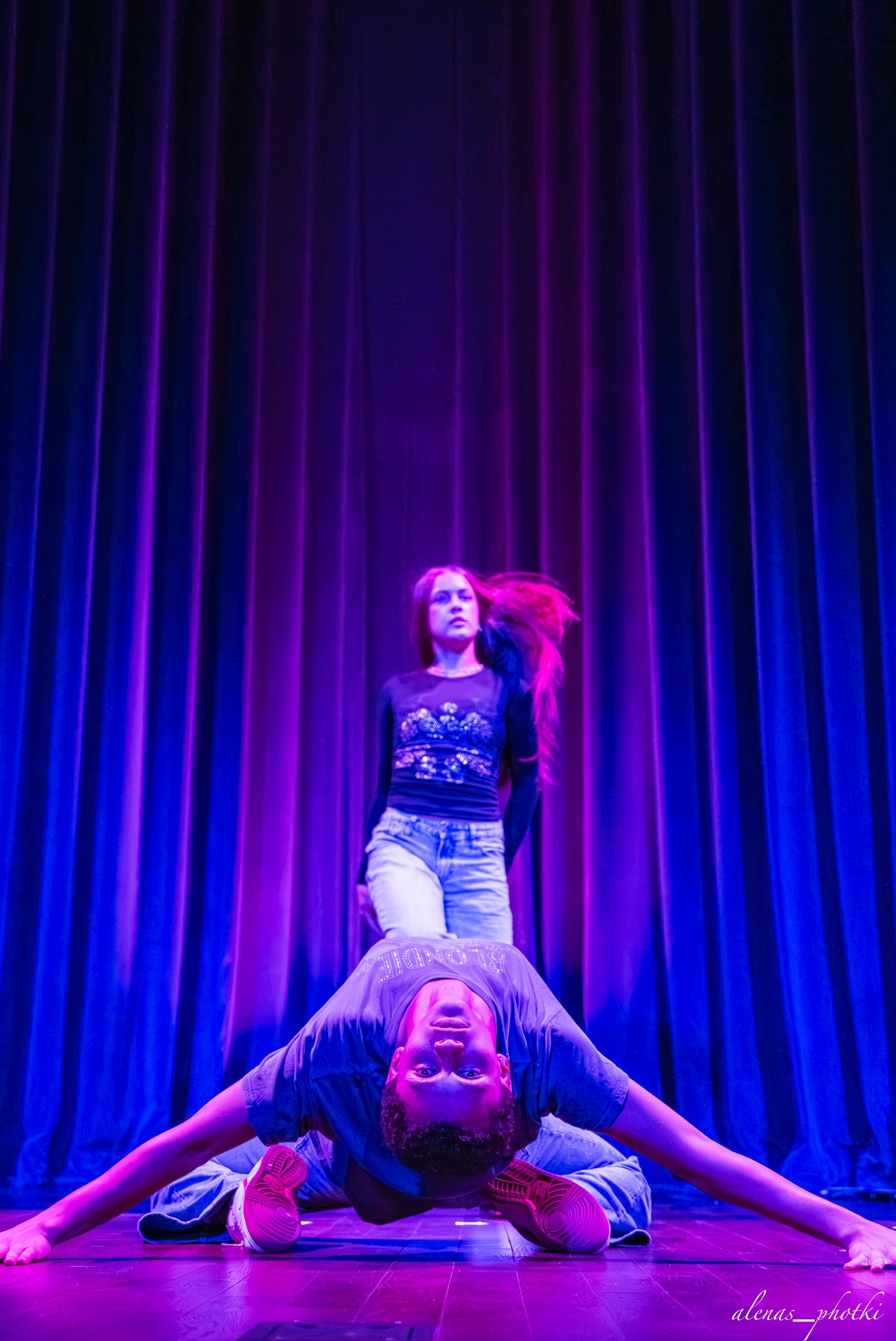 Dancer performs a split pose sequence in blue and purple stage lighting against a dark curtain backdrop.