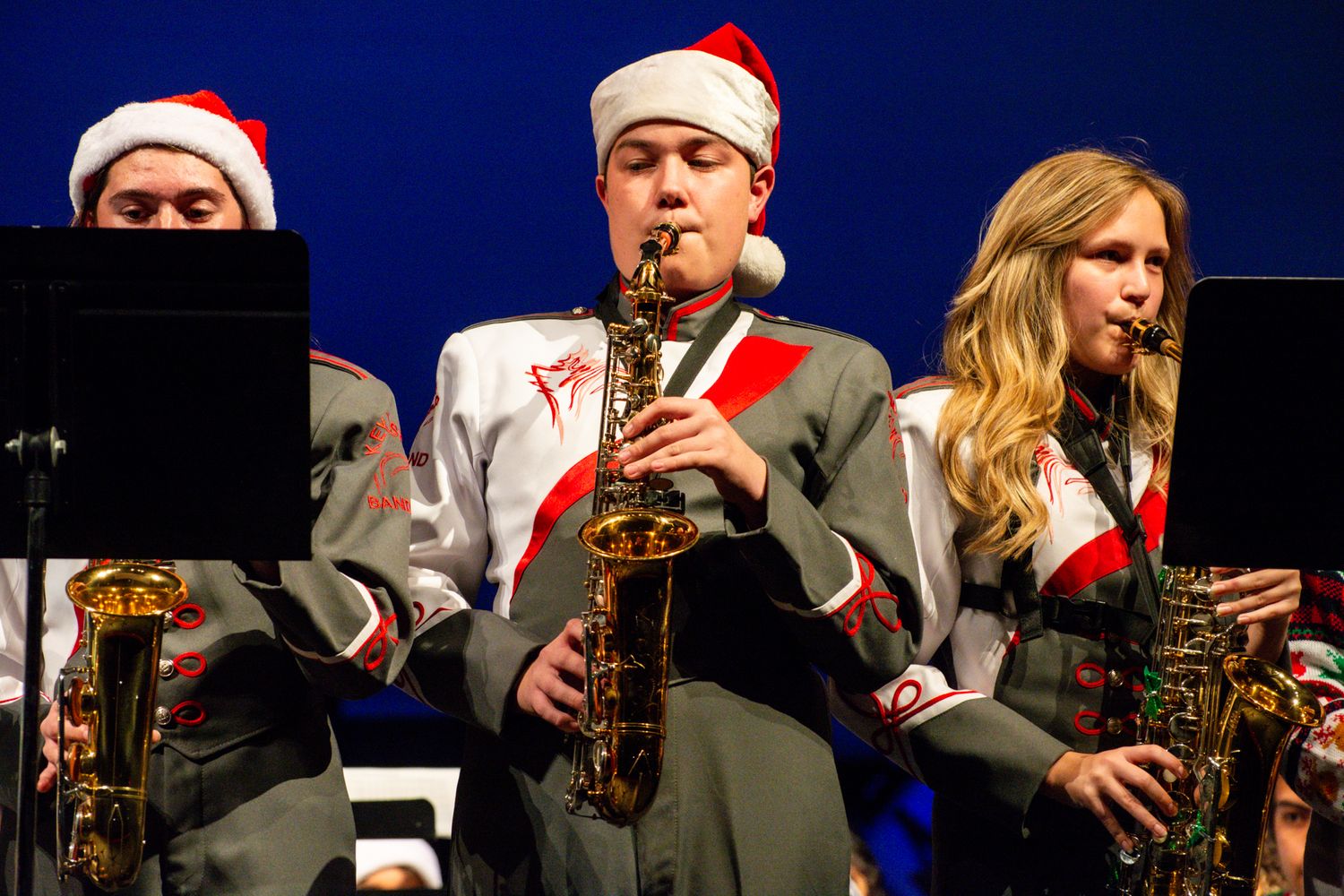 Musicians in Santa hats perform with saxophones during a holiday concert.