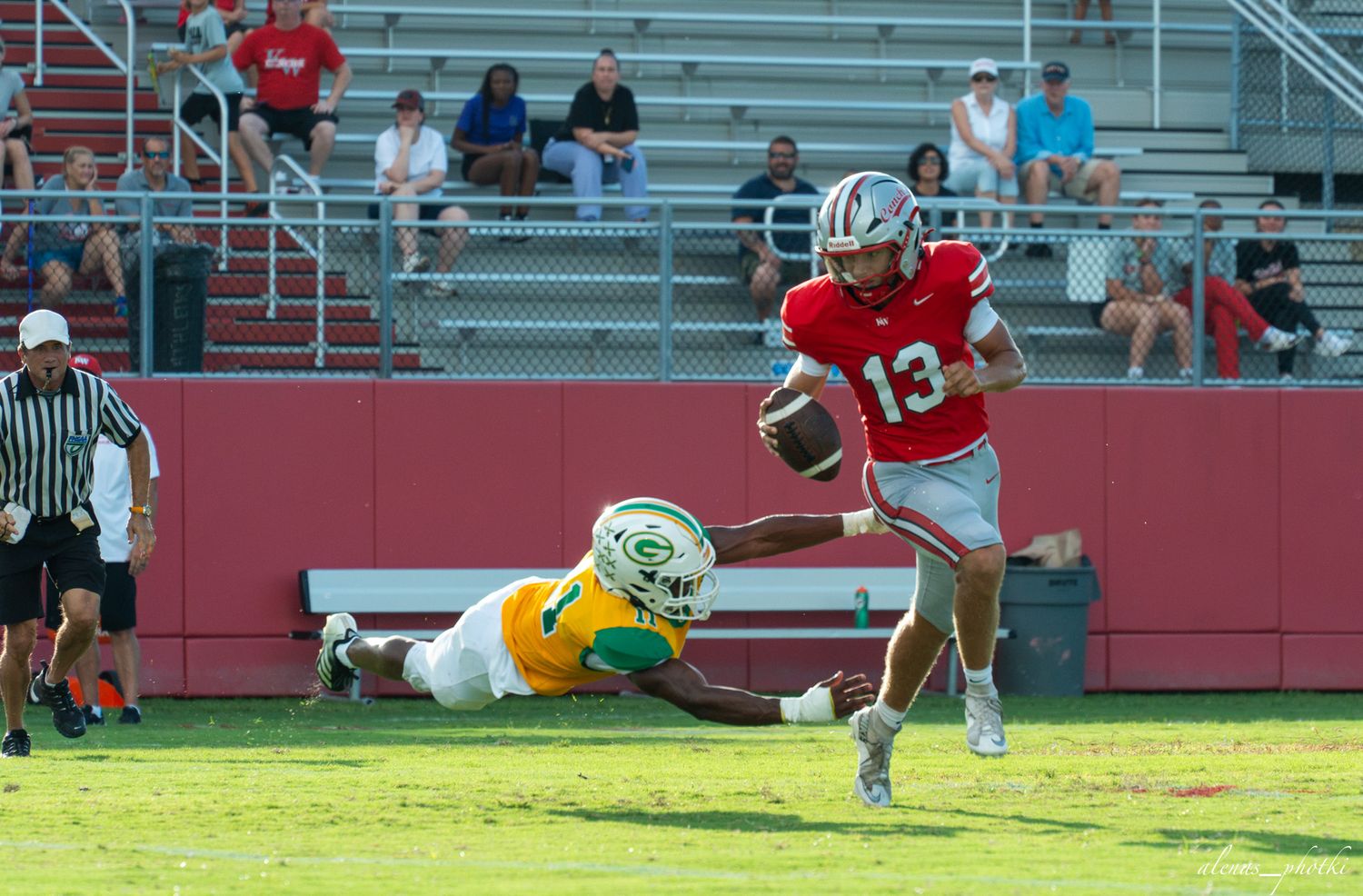 Football player #13 in red uniform evades a diving defender in yellow during a high school football game.