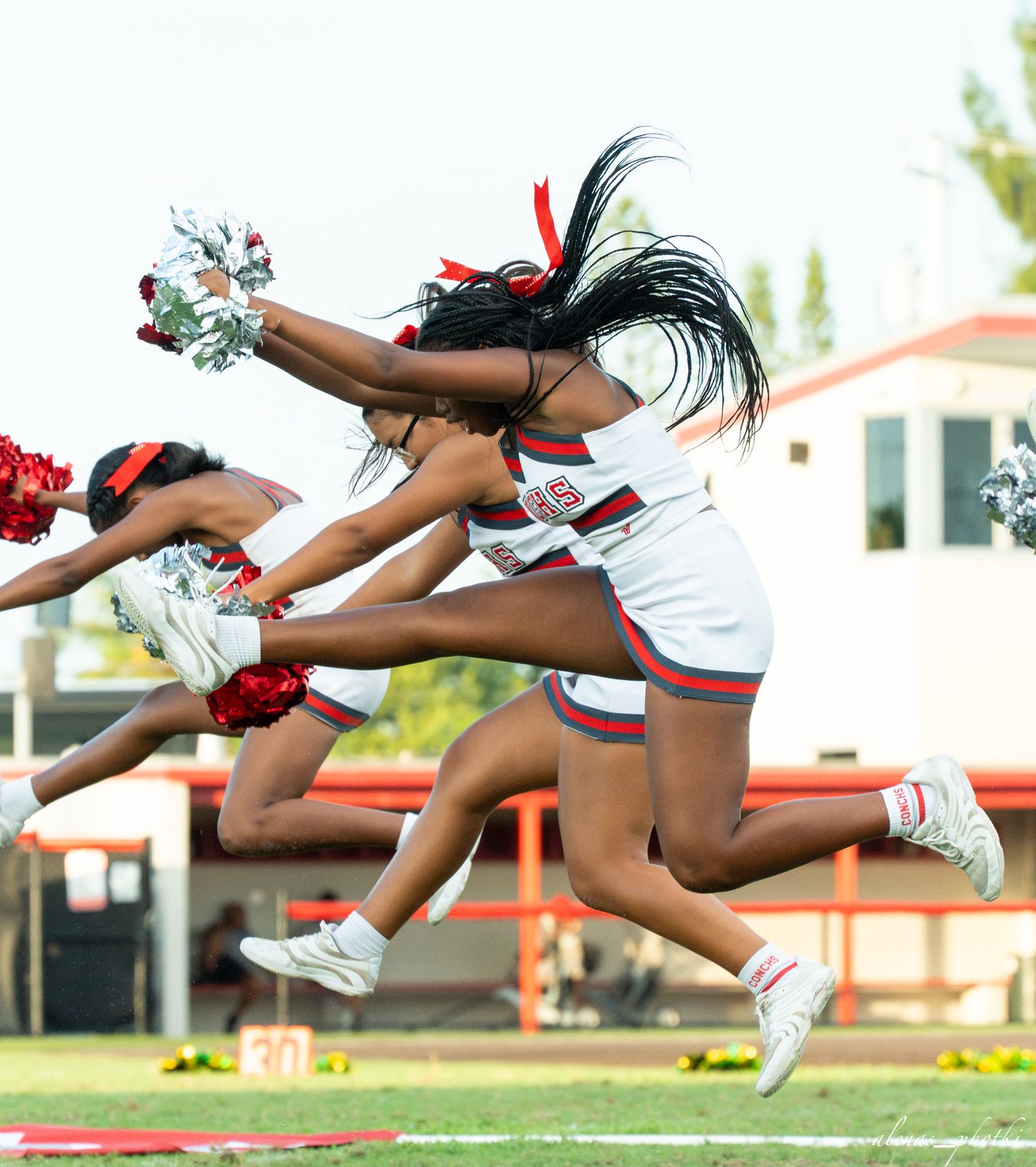 Cheerleaders in red and white uniforms leap high in the air with pom-poms during a football game.