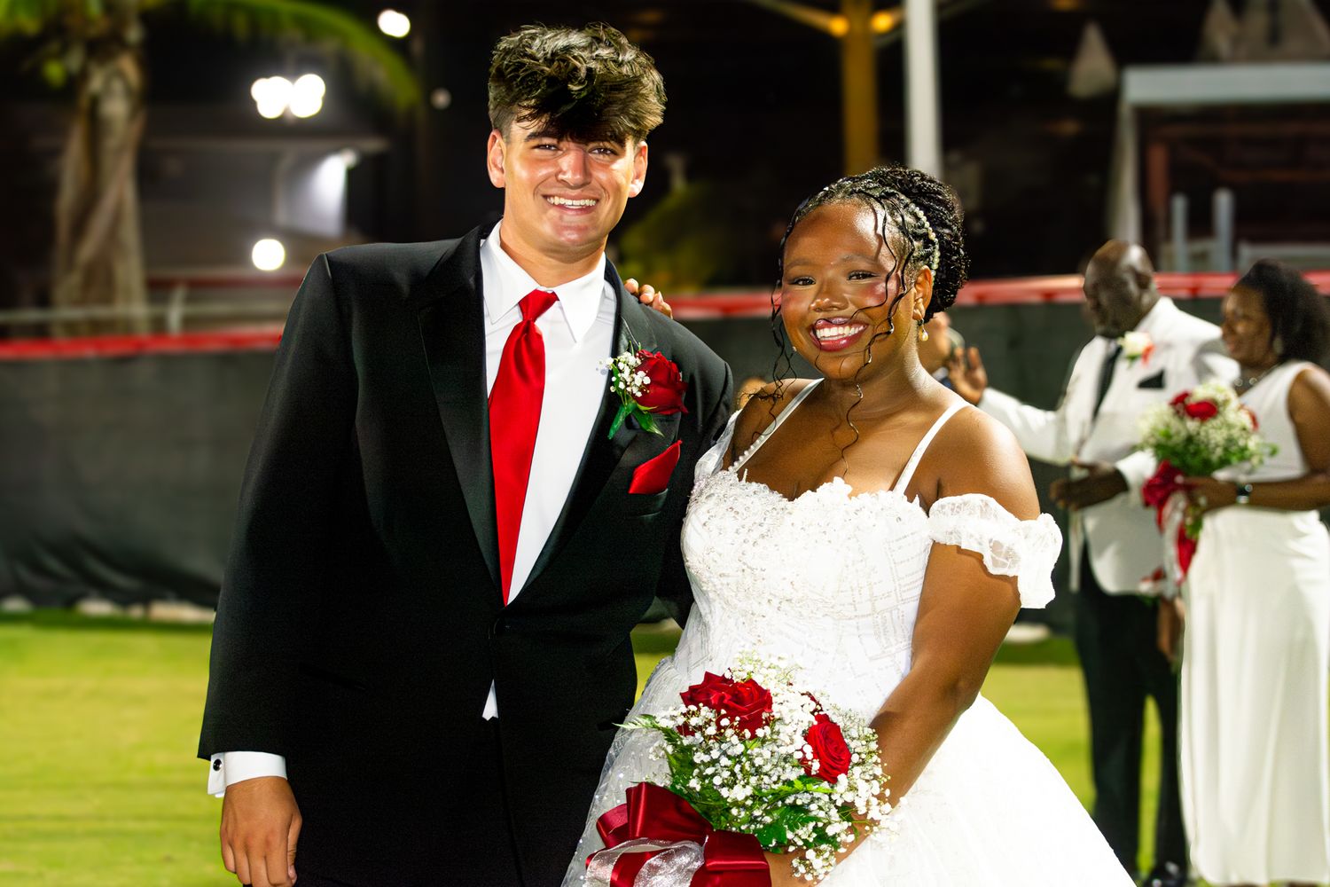 Couple in formal attire pose together at outdoor evening event.