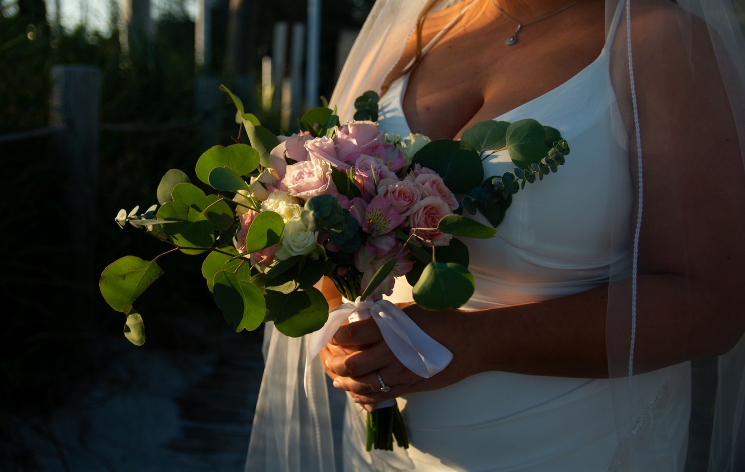 A colorful tropical wedding bouquet with orchids and roses held by hands in white.