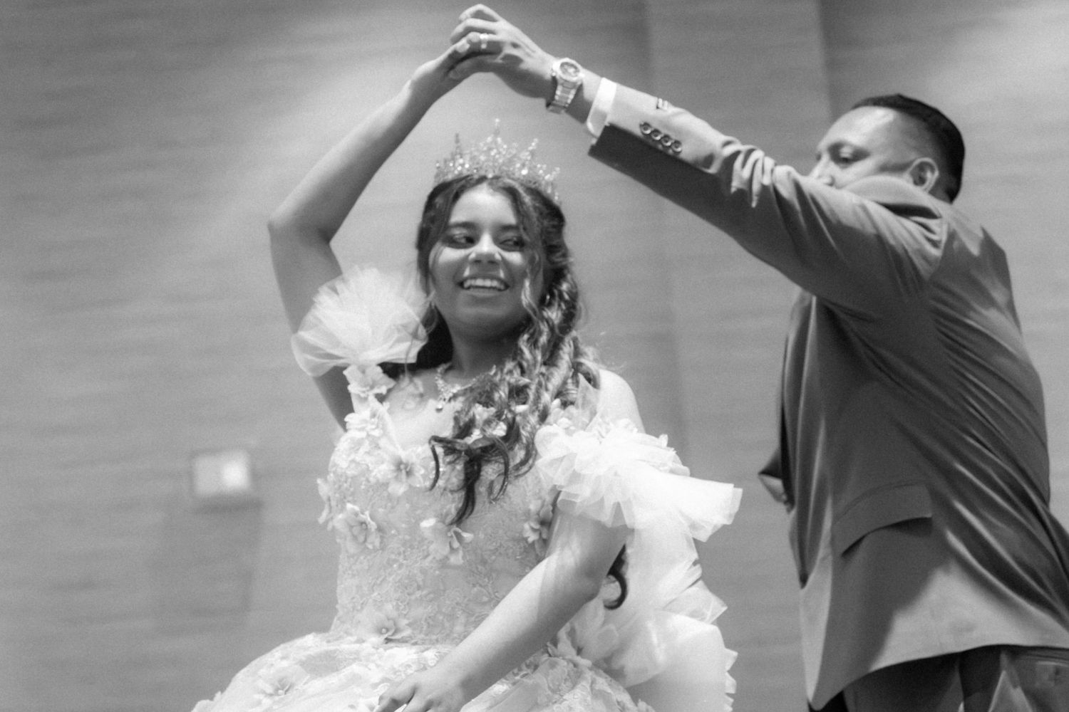 Black and white photo of a young woman in a ball gown and tiara dancing with a man at her Quinceanera.