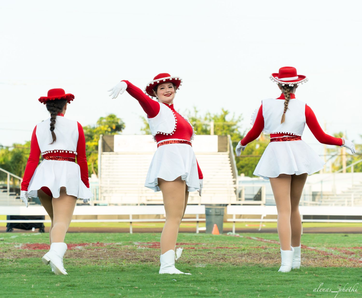 Three female majorettes in red and white uniforms perform on a green field during a marching band routine.