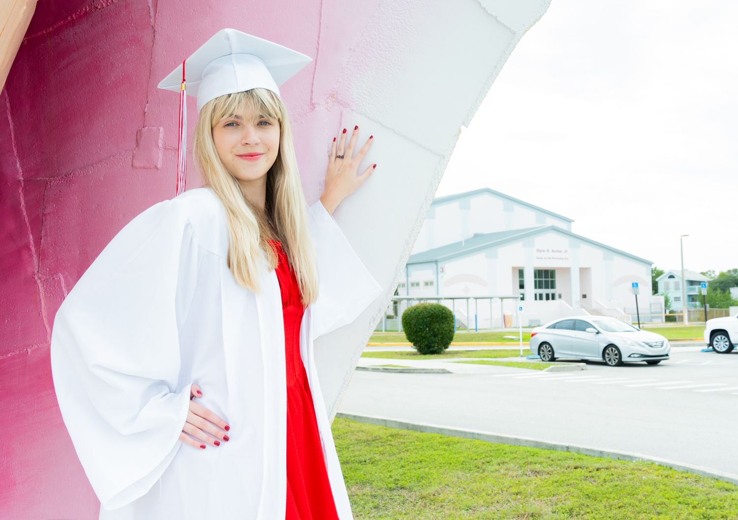 A person in a white lab coat and red dress poses outdoors against a pink wall in various positions.