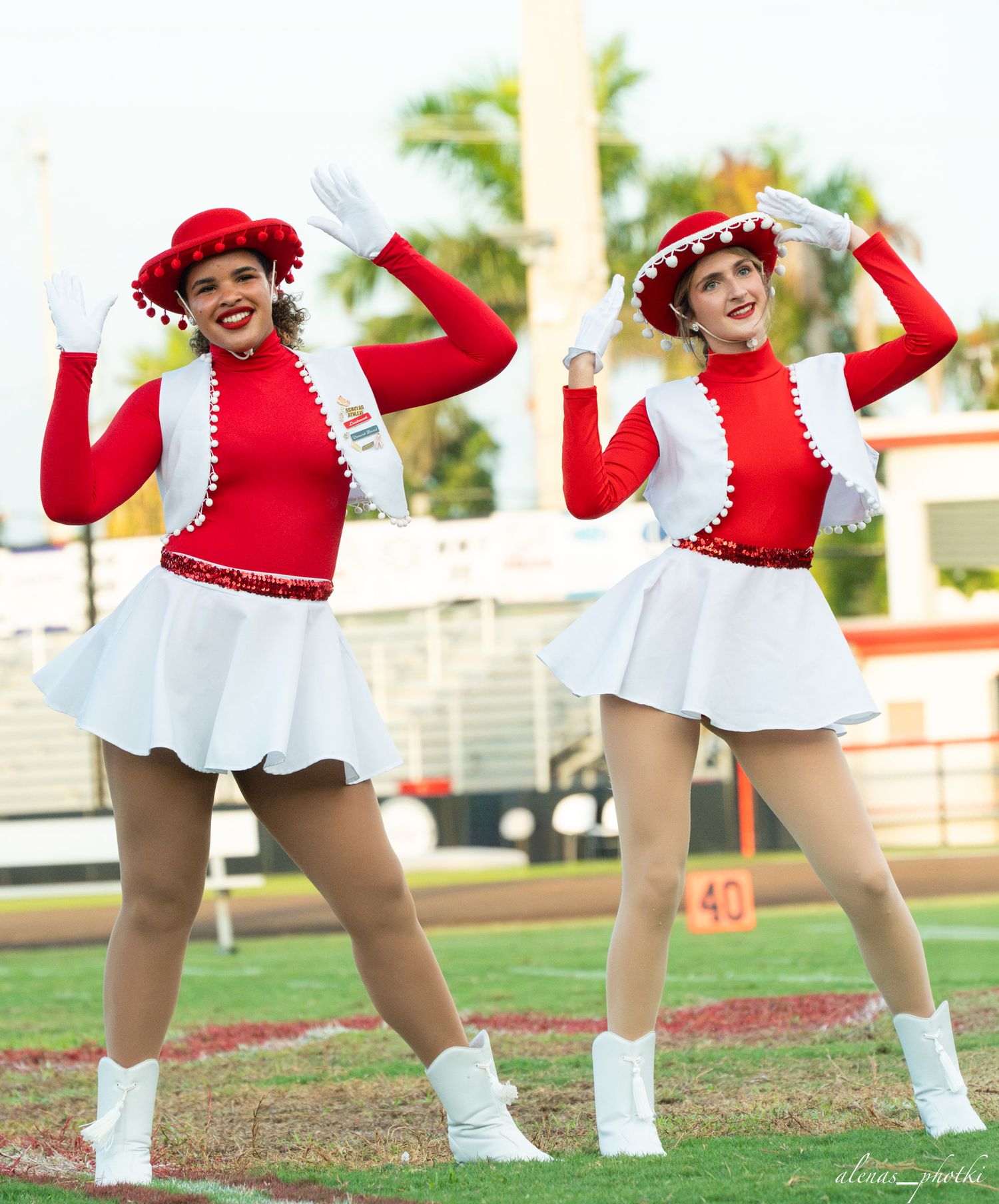 Two cheerleaders in matching red and white uniforms pose on a football field.
