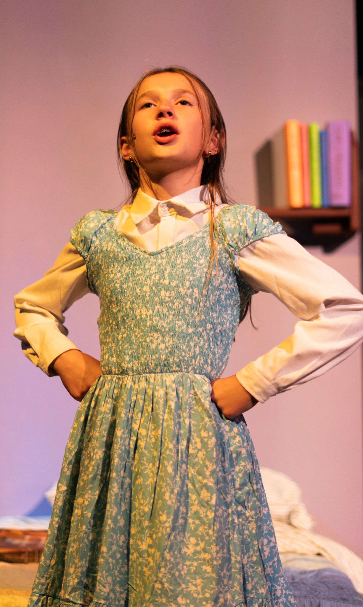 Performer in blue floral dress with white sleeves on stage in theatrical production.