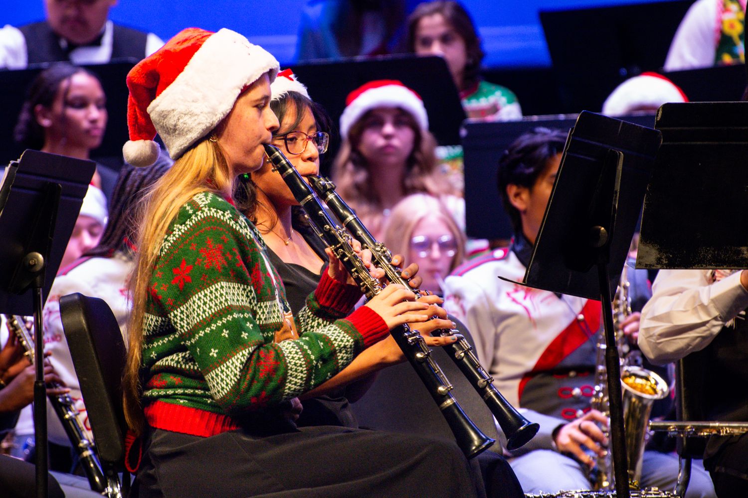 Musicians in festive holiday attire perform with woodwind instruments at seasonal concert.