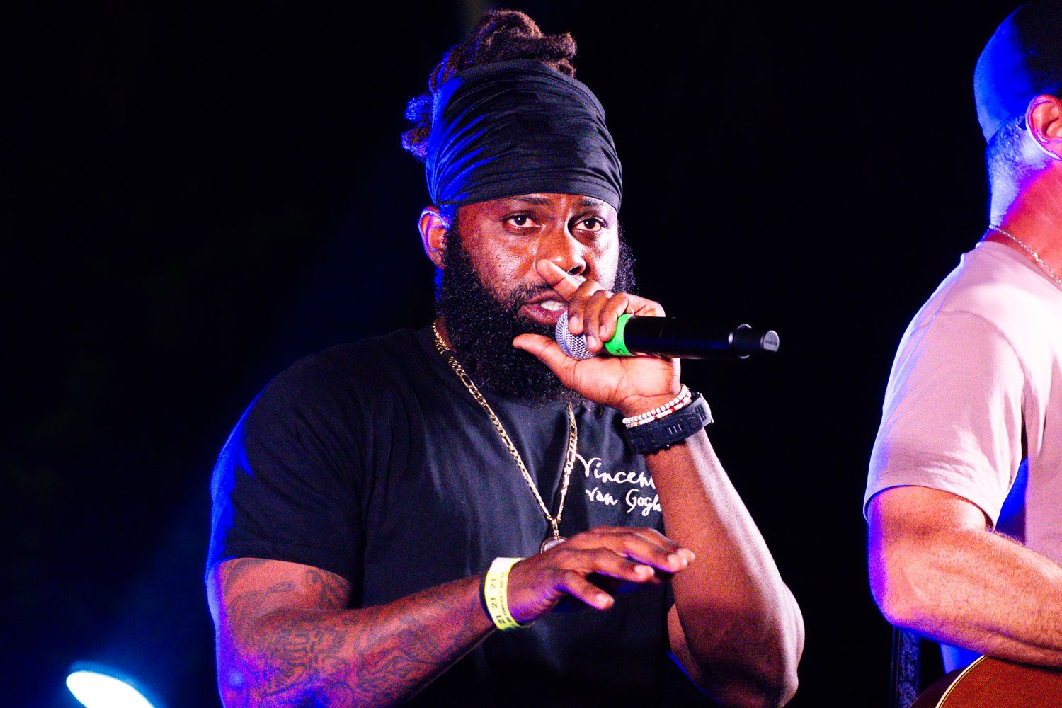 Performer in black t-shirt and beanie sings passionately into microphone on stage.