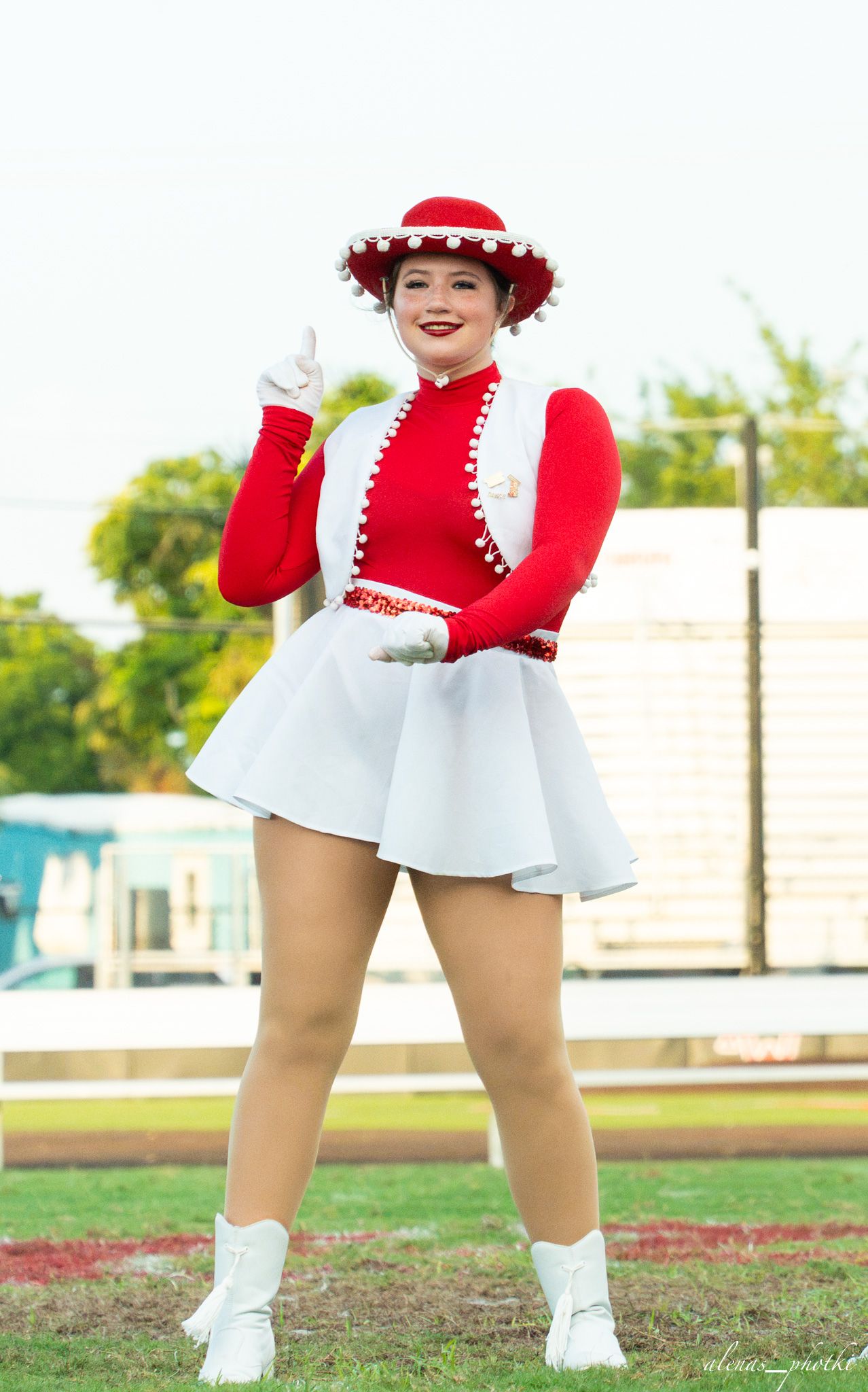 Young woman in red and white majorette uniform with matching hat poses confidently on a green field.