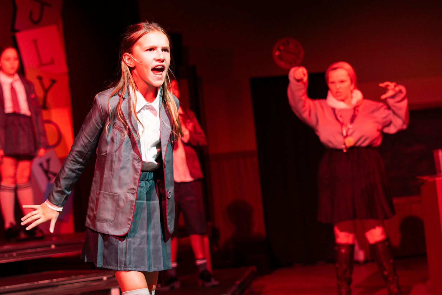 Student performer in leather jacket and uniform passionately singing during a dramatic scene.