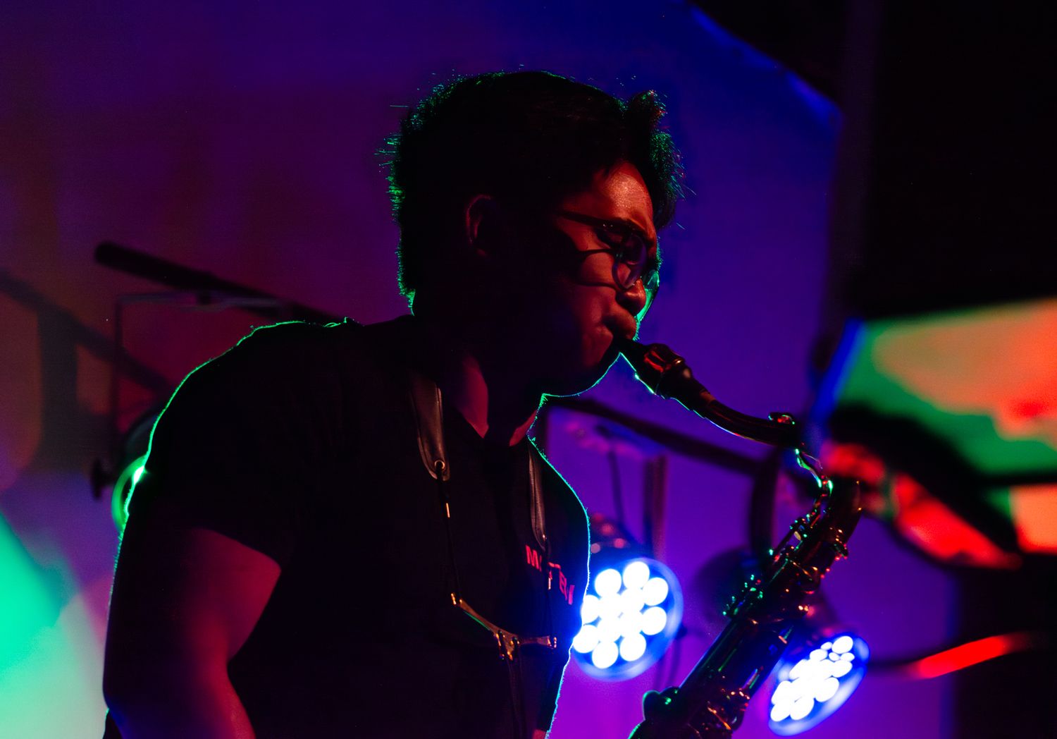 Saxophone player performs on stage with colorful blue and green lighting effects.