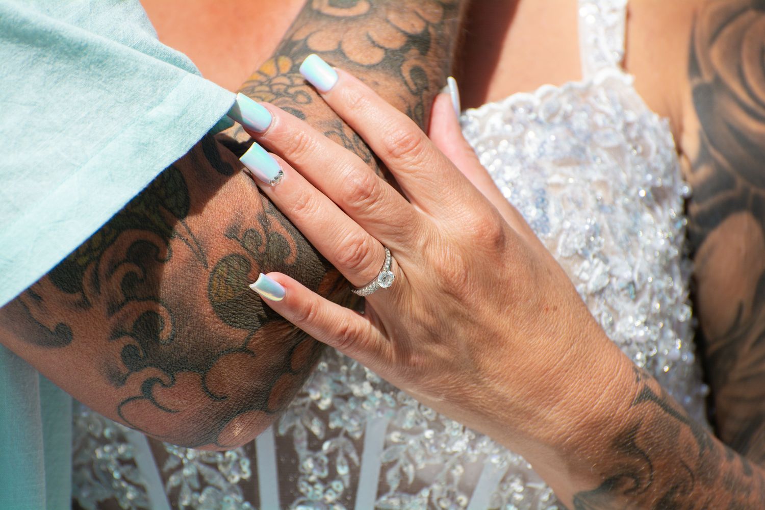Close-up of tattooed hands with wedding rings against lace dress detail.