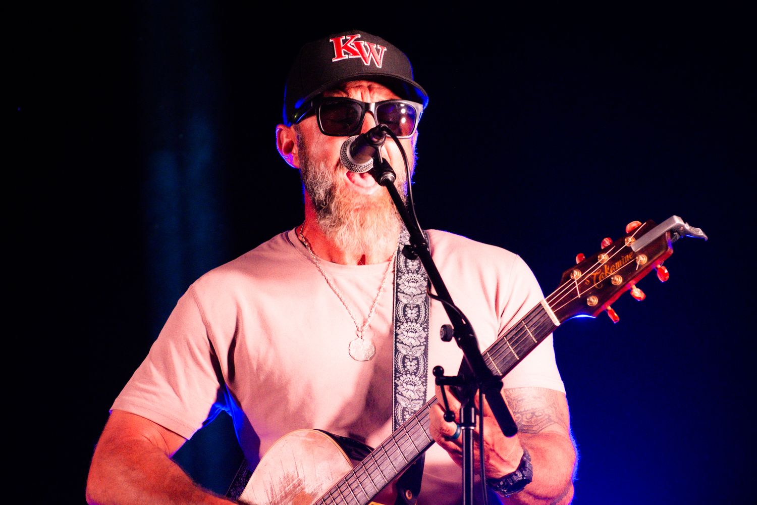 Guitarist in red cap performs on stage under dramatic lighting.