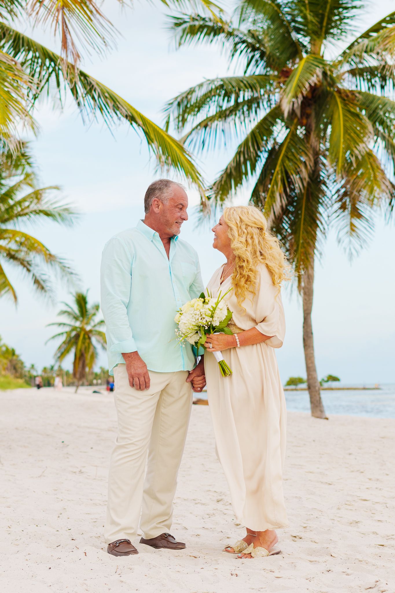 A romantic moment between a couple on a palm-lined beach with tropical flowers.