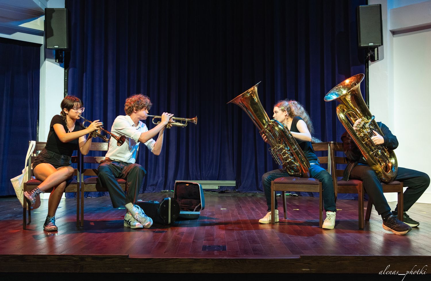 Musicians perform an energetic choreographed dance routine while playing brass instruments on stage.