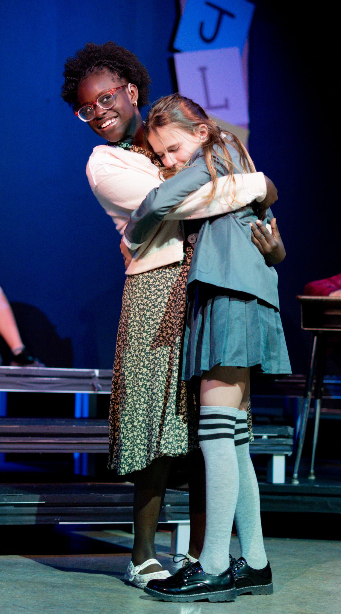A touching moment between performers in a school play with striped socks and vintage costumes.