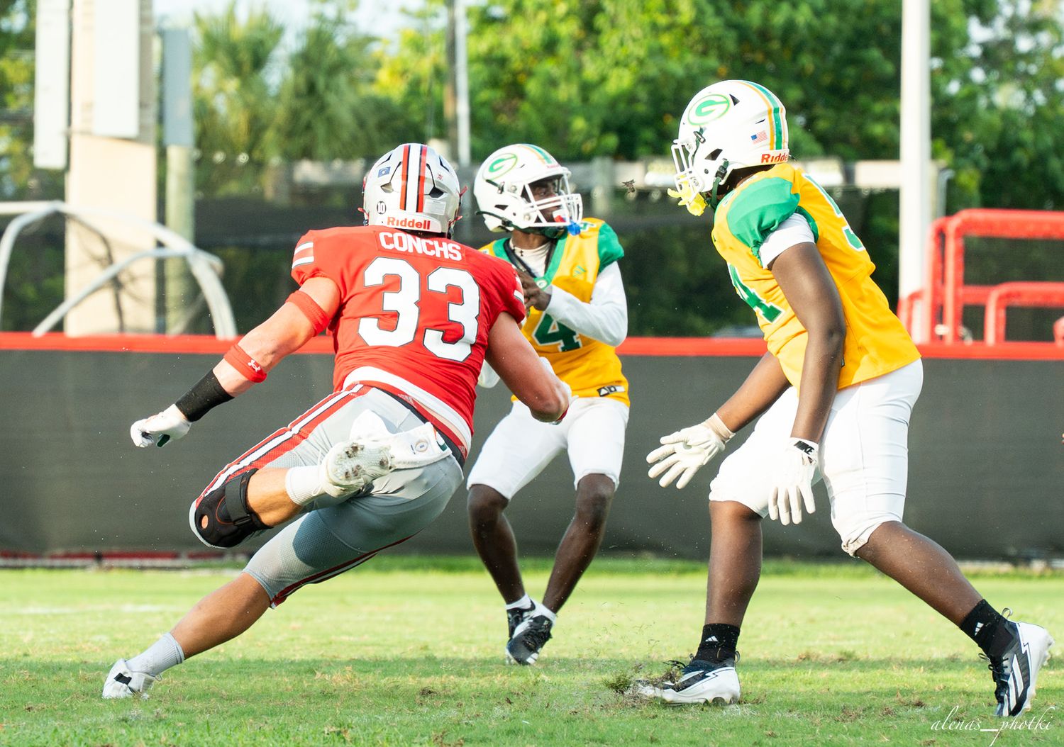 Football players in red and yellow uniforms compete during a practice scrimmage on an outdoor field.