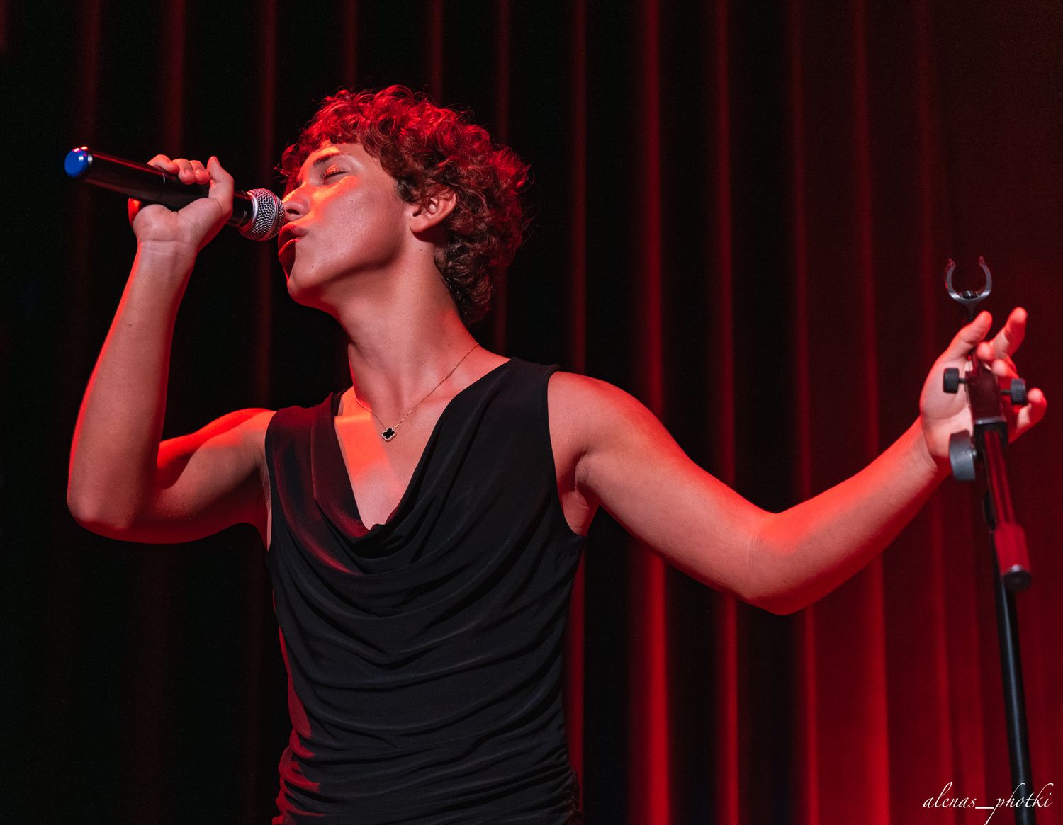 Performer in black attire silhouetted against red stage lighting during dramatic performance.