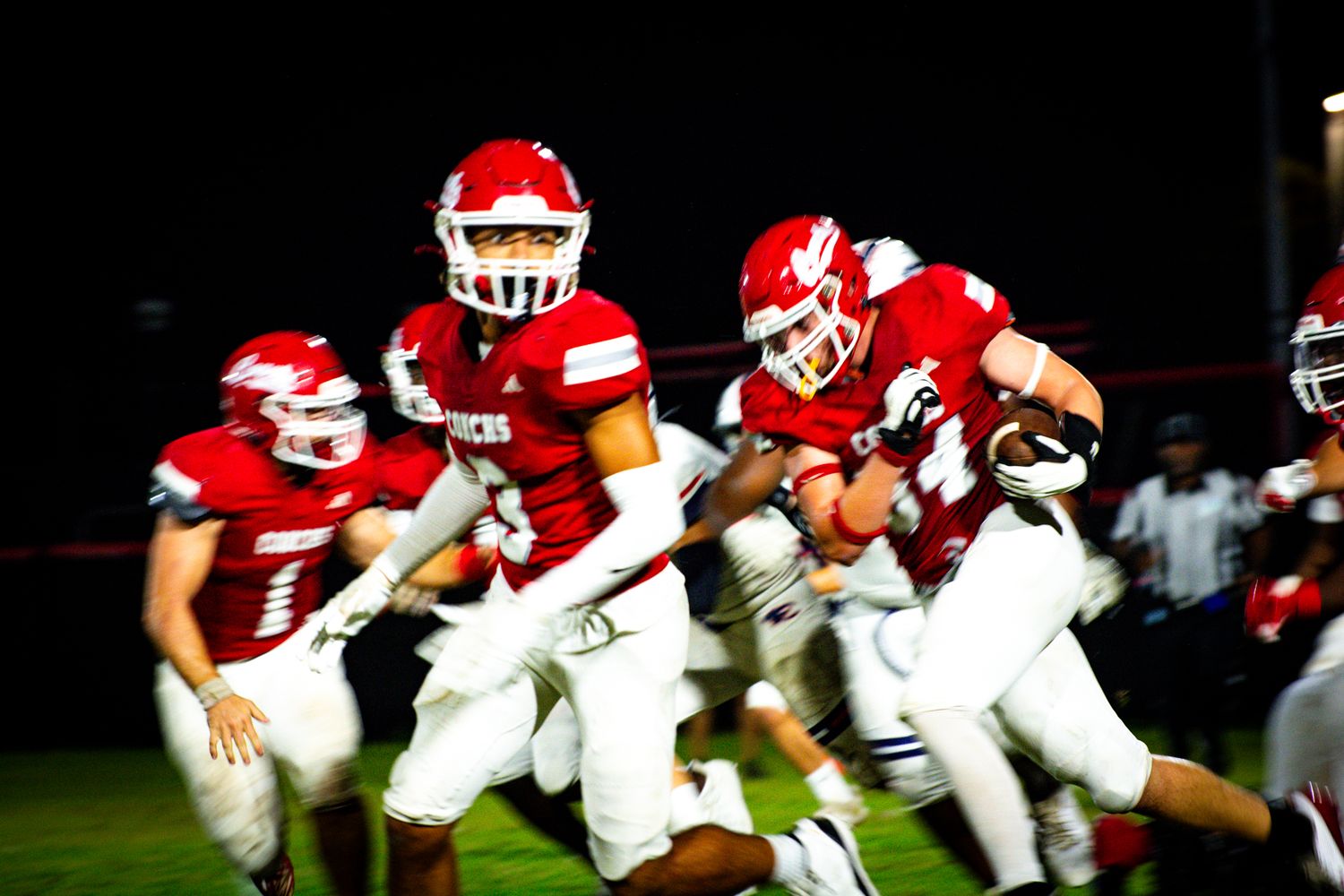 Football players in red helmets and white jerseys charge forward during gameplay.