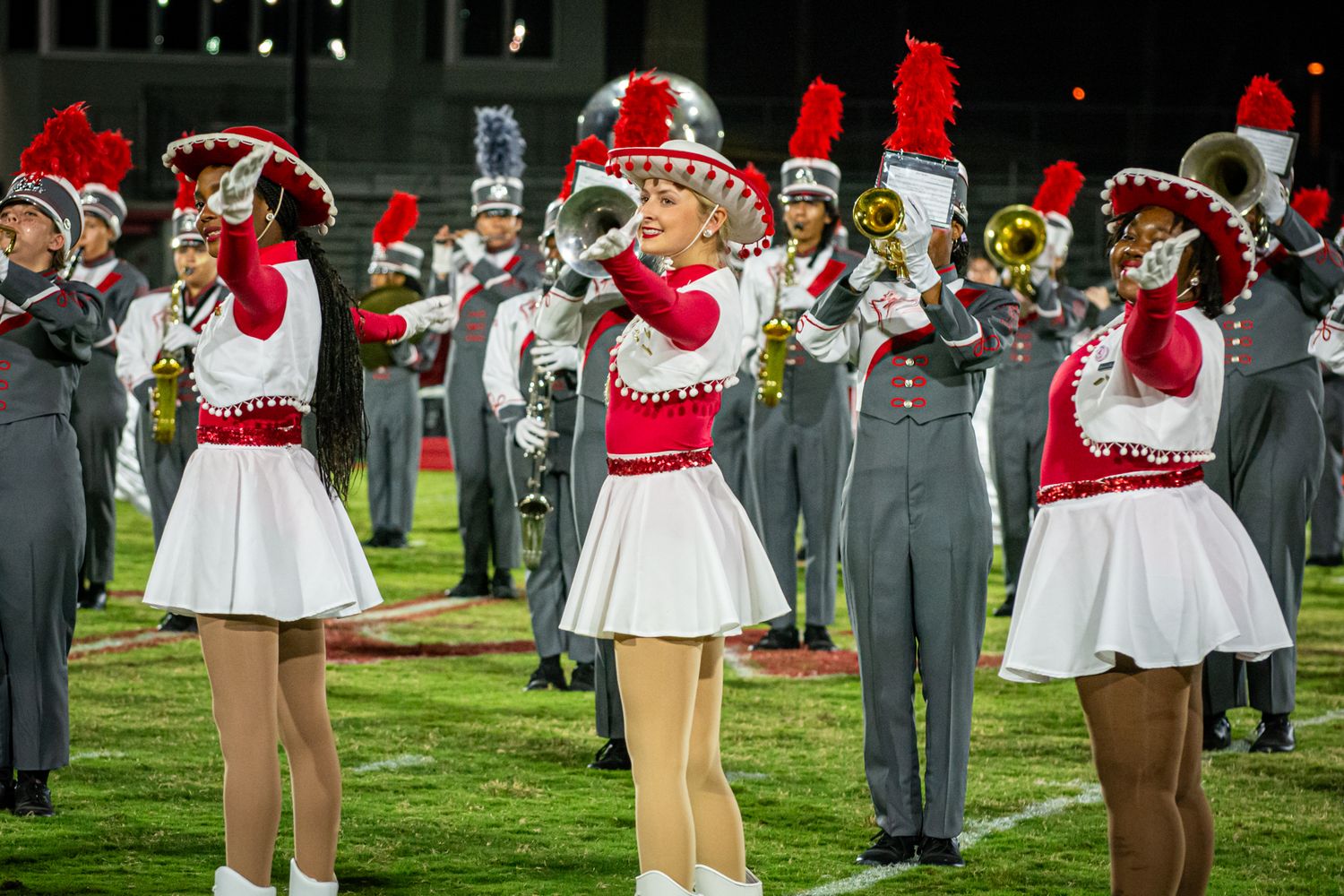 Marching band members in red and white uniforms perform on a grass field.