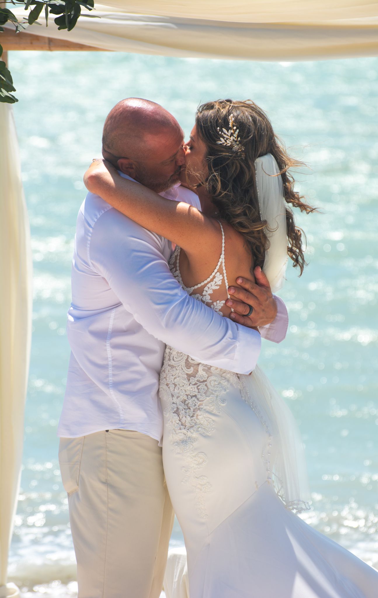 A romantic beach wedding kiss with sparkling turquoise water in the background.