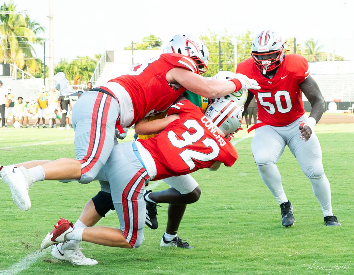 College football players in red uniforms tackle opponent #32 on green field during competitive game.