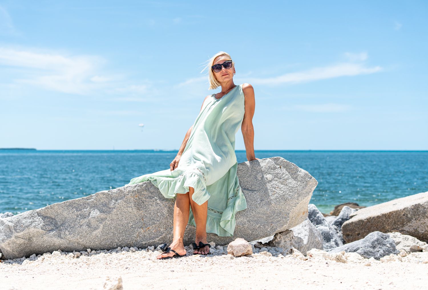 A casual summer scene with someone in a mint dress posing on coastal rocks by the ocean.