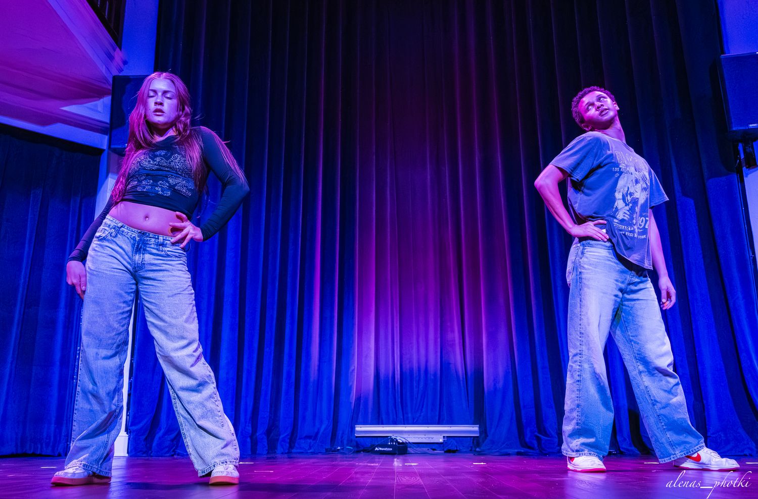 Dancers in white outfits perform on stage with dramatic blue lighting during a contemporary dance performance.