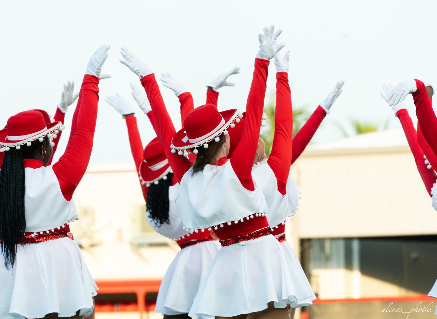 Young women in red and white uniforms with matching hats perform a dance routine with arms raised high.