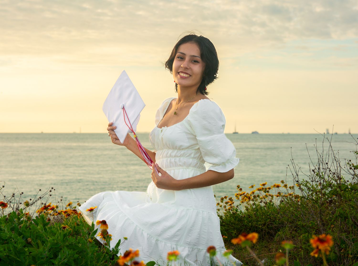 Woman in white dress holds paper while standing in wildflower field at sunset.