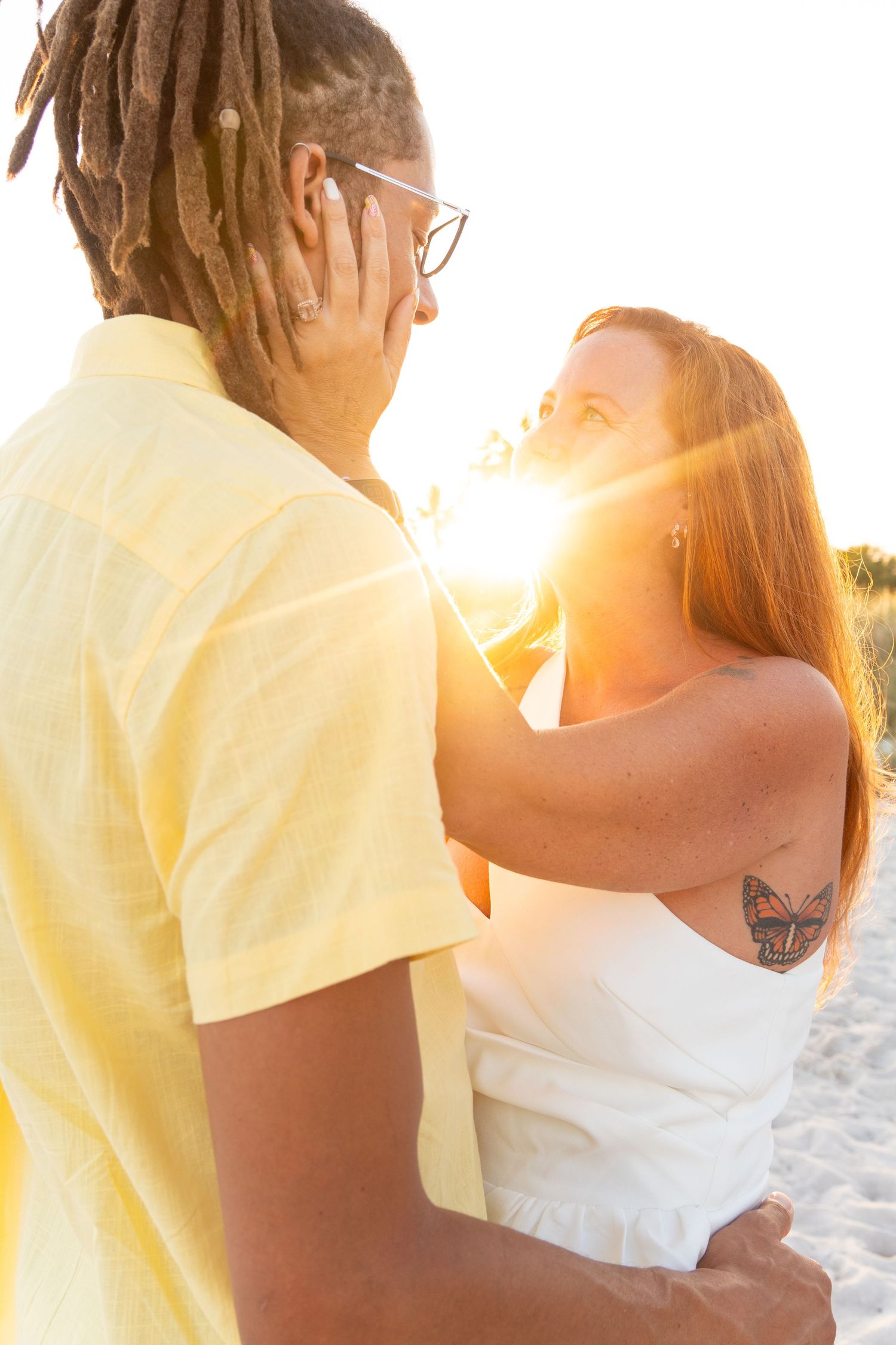 Couple sharing a romantic moment at sunset on the beach, woman touching man's face with sun flare.