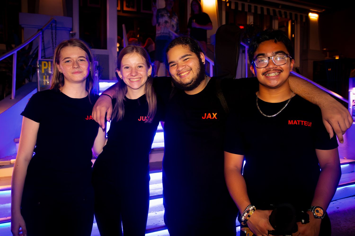 Event staff in black uniforms pose together against illuminated blue background.
