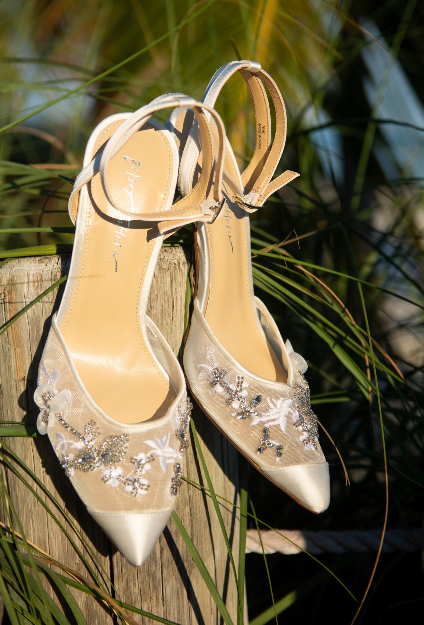 Elegant bridal shoes with crystal embellishments displayed against tropical foliage.