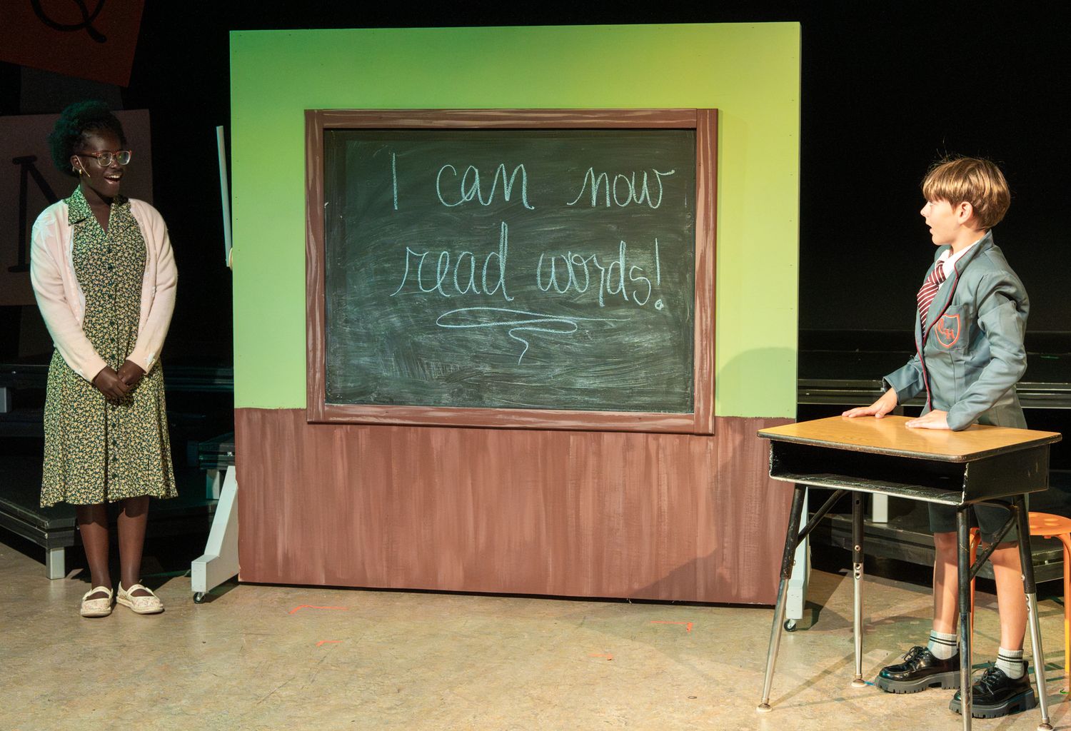School play set with chalkboard and classroom props against green backdrop.